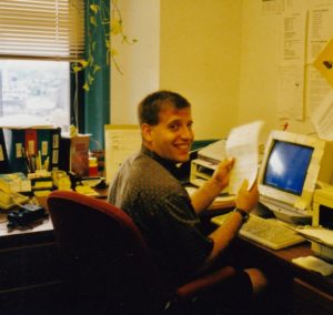 Image of Anthony Galasso sitting a computer desk and smiling